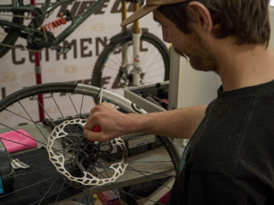 Mecánico ajustando el disco de freno de una rueda de bicicleta de montaña sobre una mesa de trabajo.