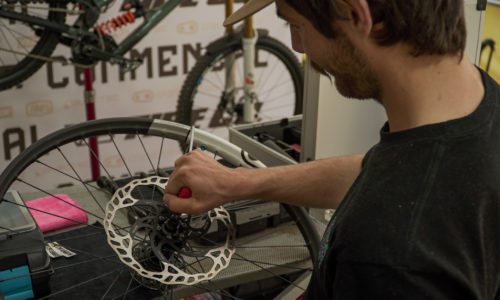 Mecánico ajustando el disco de freno de una rueda de bicicleta de montaña sobre una mesa de trabajo.