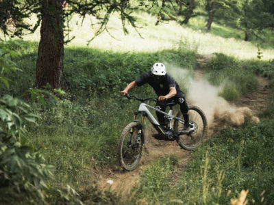 Ciclista descendiendo a toda velocidad por un sendero de montaña, levantando polvo entre los árboles.