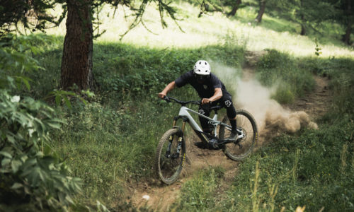 Ciclista descendiendo a toda velocidad por un sendero de montaña, levantando polvo entre los árboles.